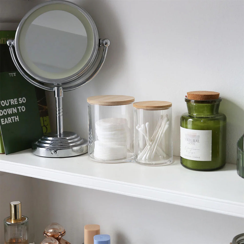 Makeup mirror and storage jars on a shelf with a book in the background